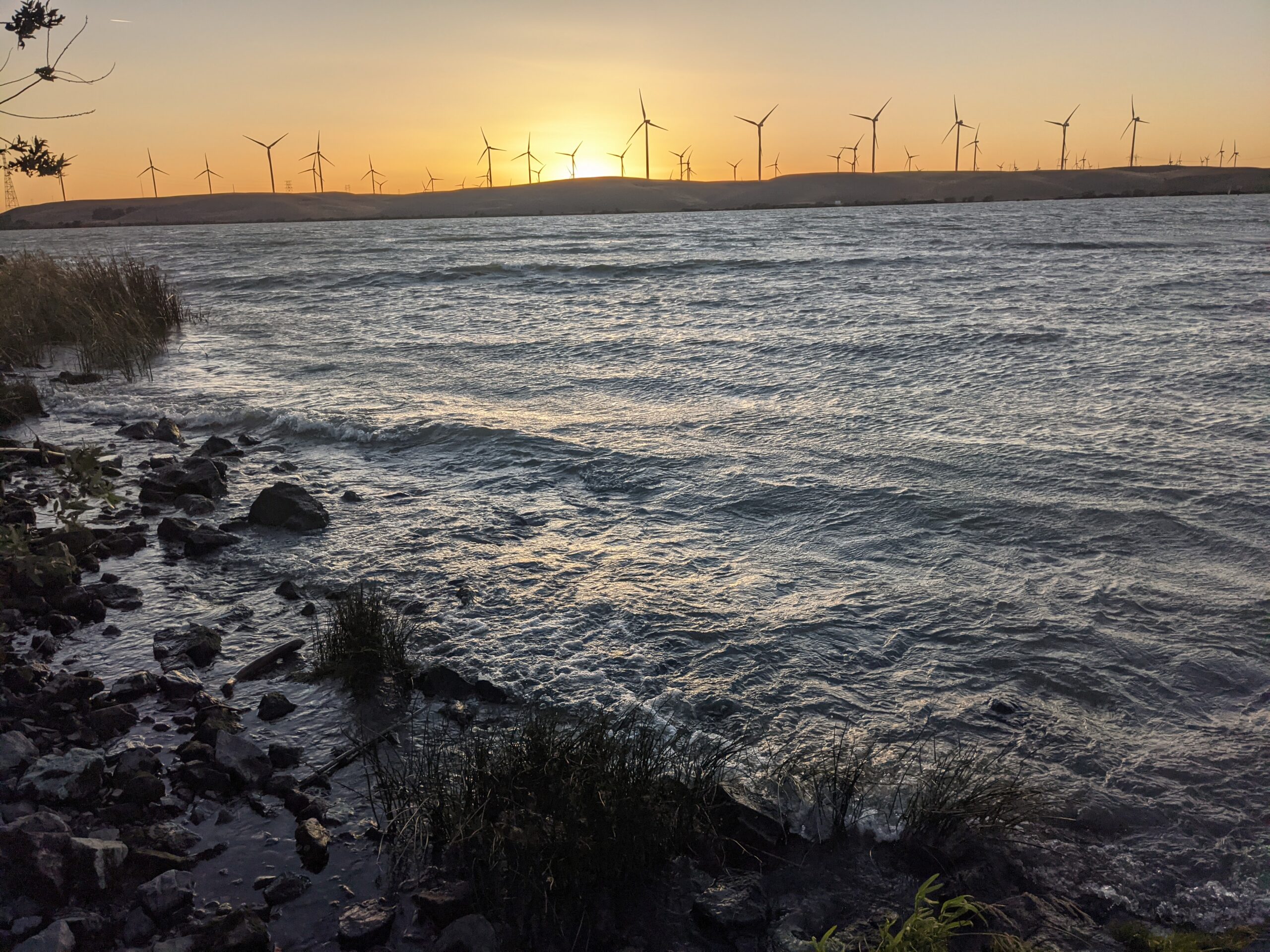 Sunset over the Sacramento River at Rio Viento, with the Montezuma Hills wind turbines on the far bank